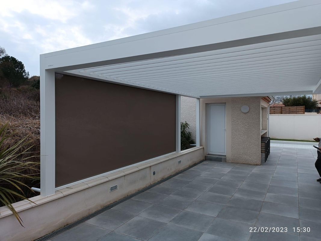 Pergola blanche, terrasse carrelée grise, petit bâtiment et aménagement extérieur.