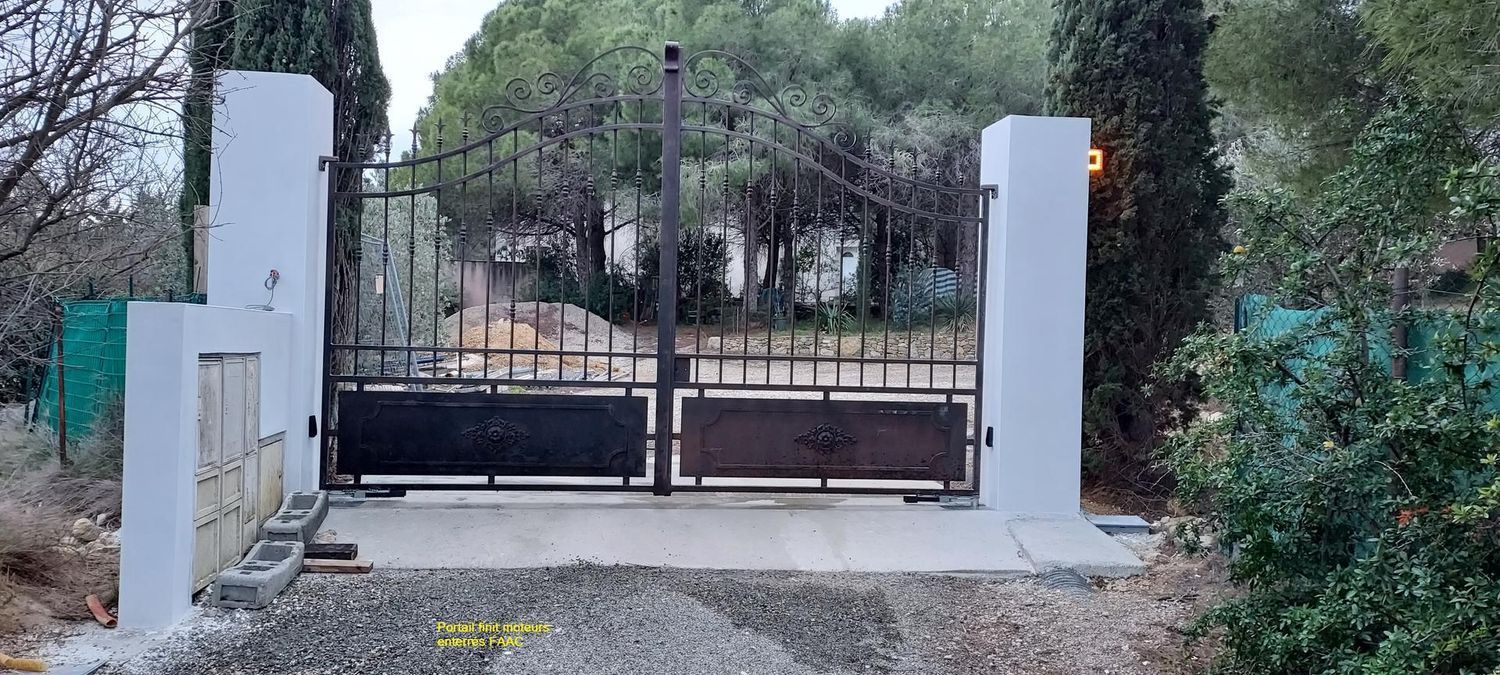 Un portail métallique à deux vantaux, encadré par des piliers blancs. Gravier et arbres en arrière-plan.