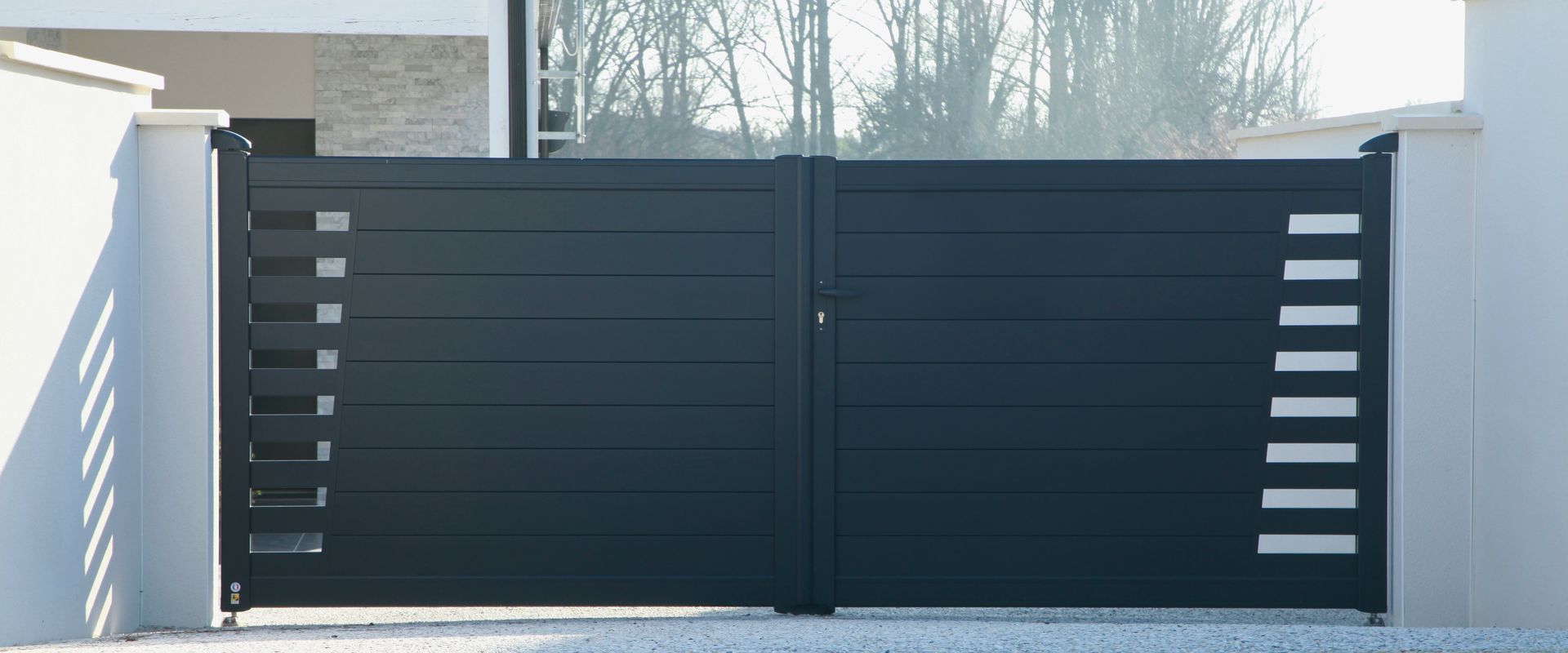 Portail fermé, avec découpes rectangulaires sur piliers blancs.