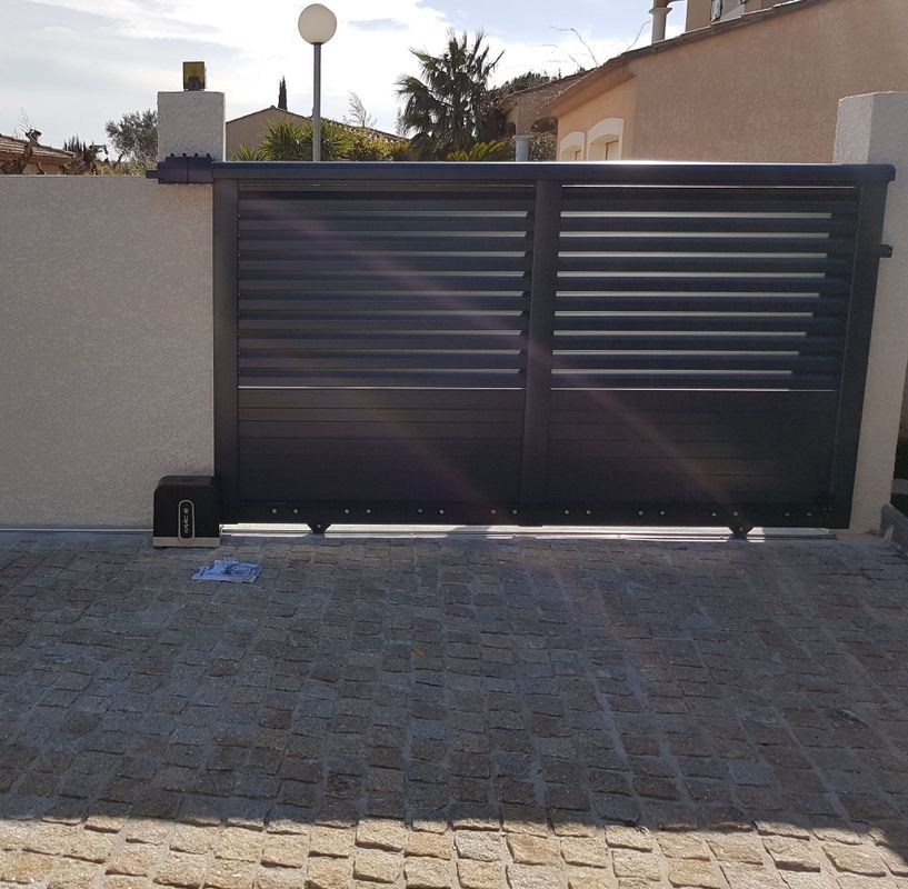 Portail coulissant gris foncé sur une allée pavée.