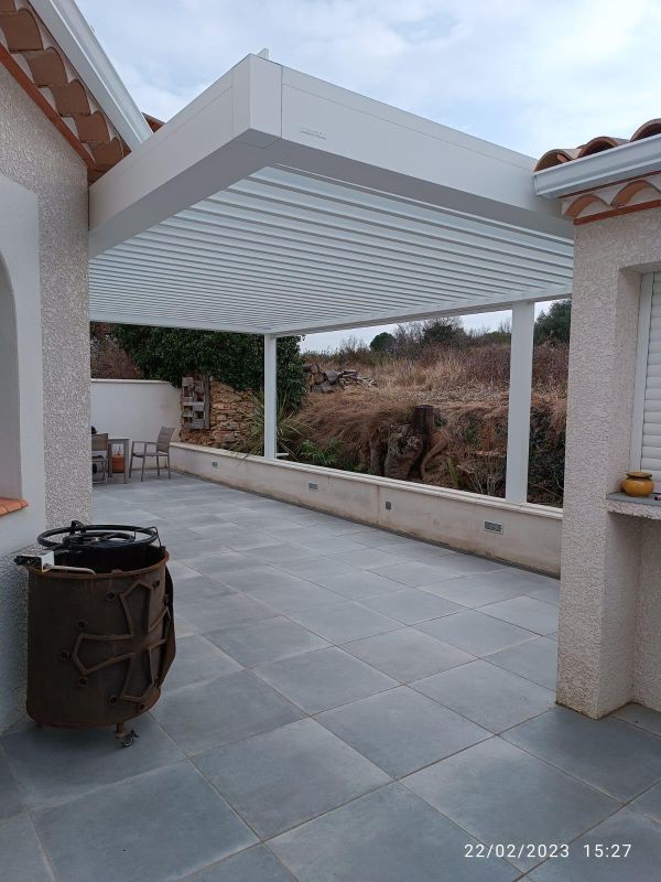 Une terrasse avec une pergola blanche, un sol carrelé gris et une vue sur une colline.