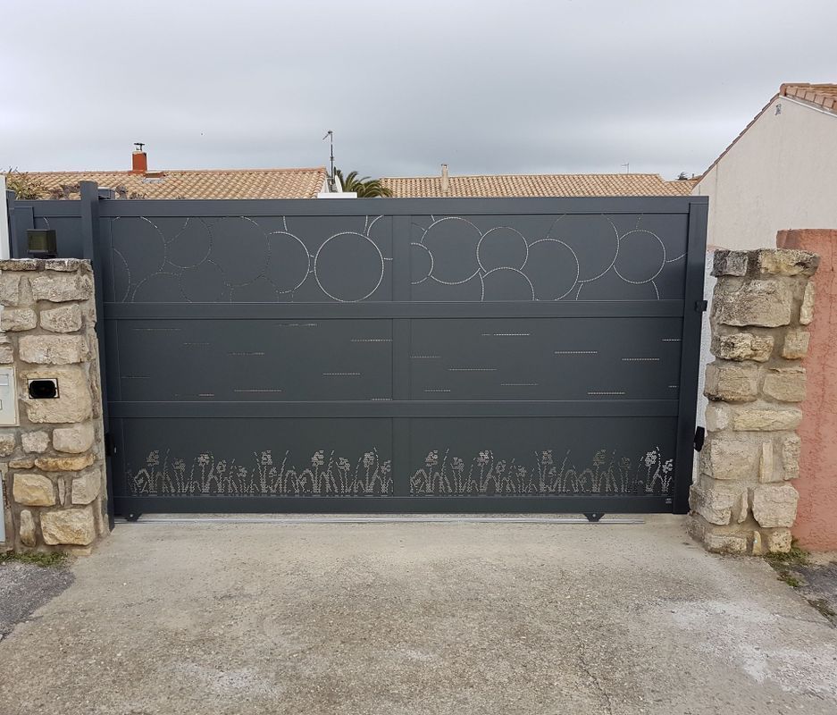 Portail coulissant gris orné de découpes florales et circulaires.