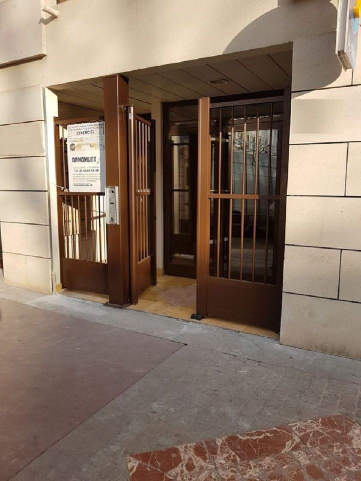 Entrée d'un bâtiment avec des portes en métal marron, des murs en briques beiges et une allée carrelée.
