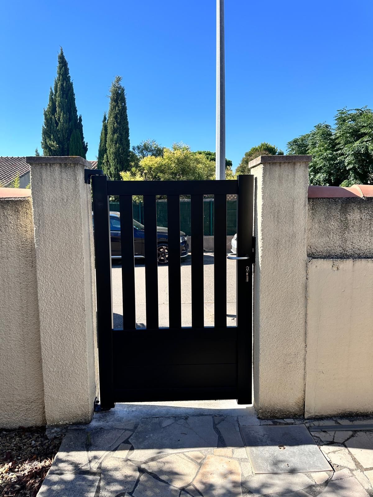 Un portail noir entre des piliers de béton, menant à une propriété.