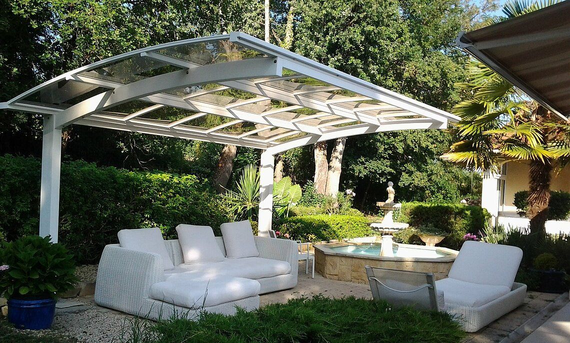 Mobilier de jardin blanc sous un carport blanc, dans un jardin avec une fontaine.
