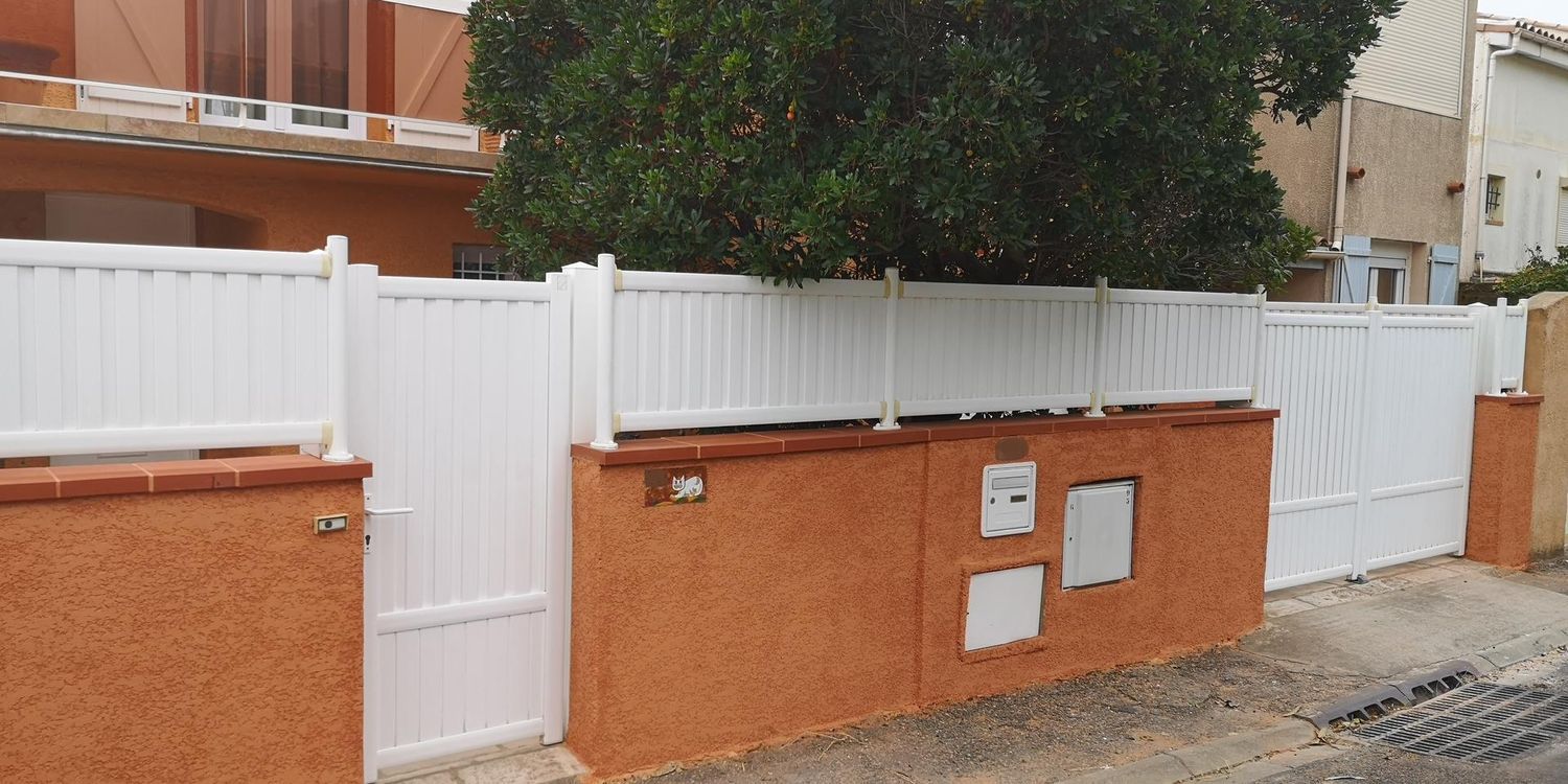 Portail et clôture blancs, avec des arbres en arrière-plan.