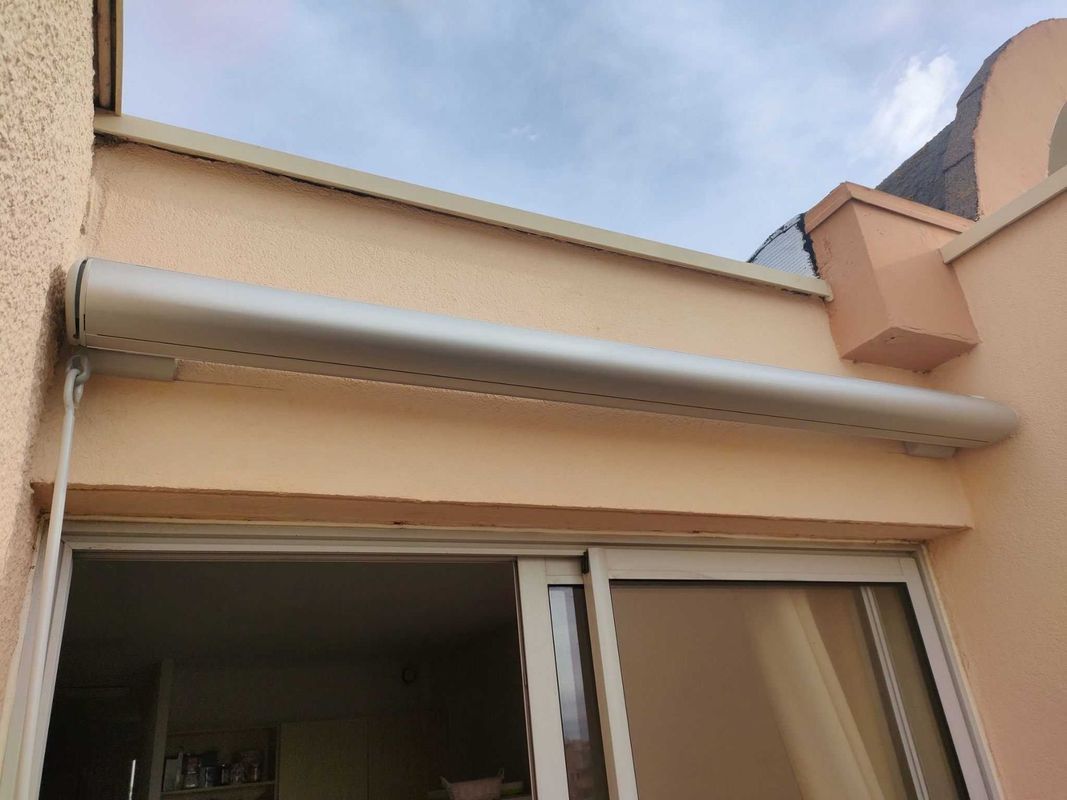 Auvent beige au-dessus d'une porte-fenêtre coulissante. Façade d'immeuble beige crème.