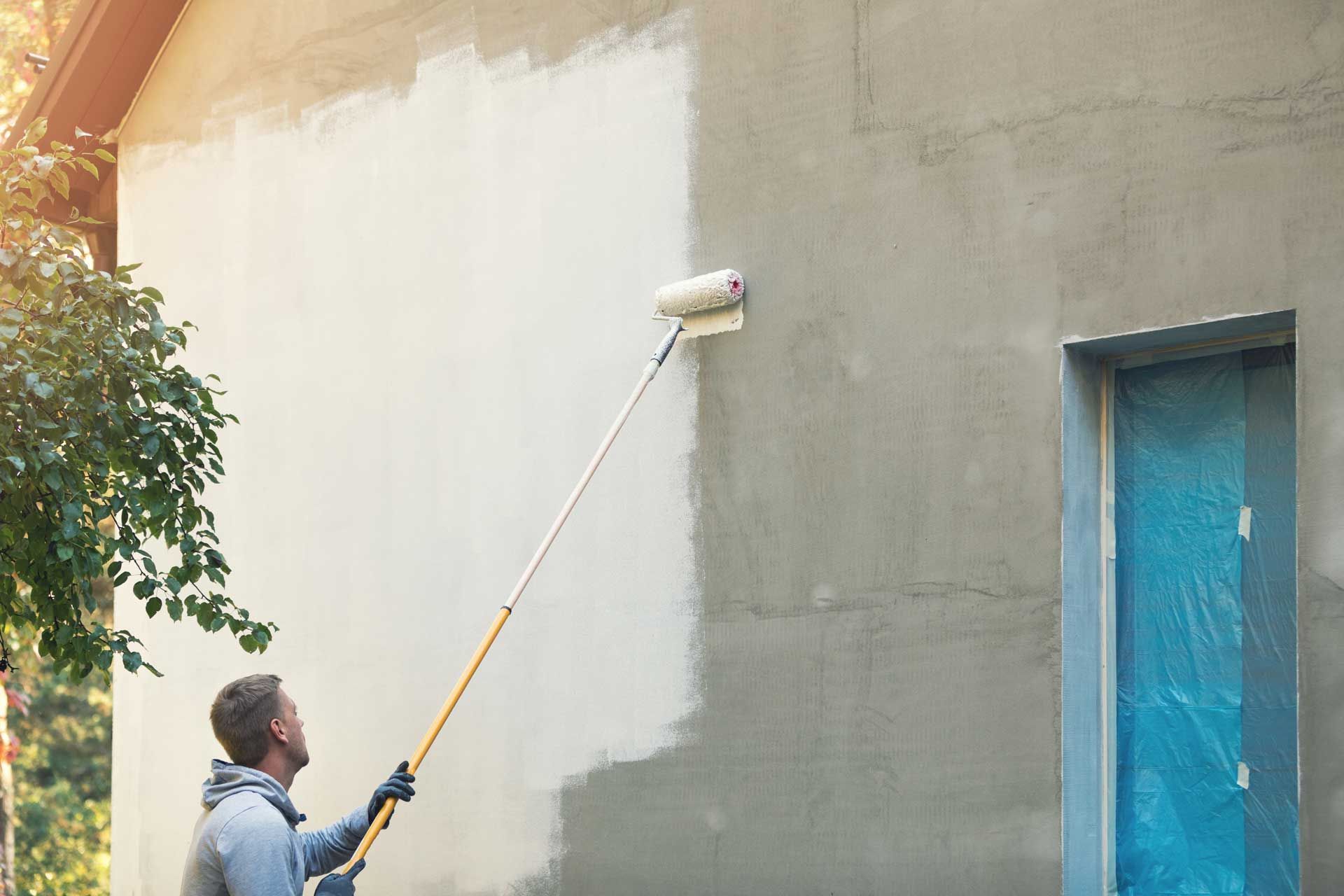 Peintre avec un rouleau et une perche au travail sur un mur extérieur d’une maison