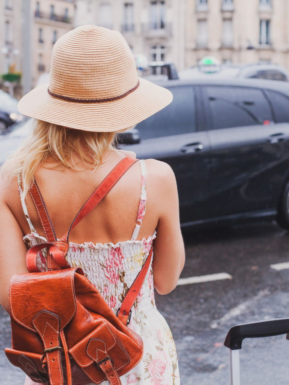 Une femme de dos avec un chapeau portant un sac à dos attend un taxi au bord de la route