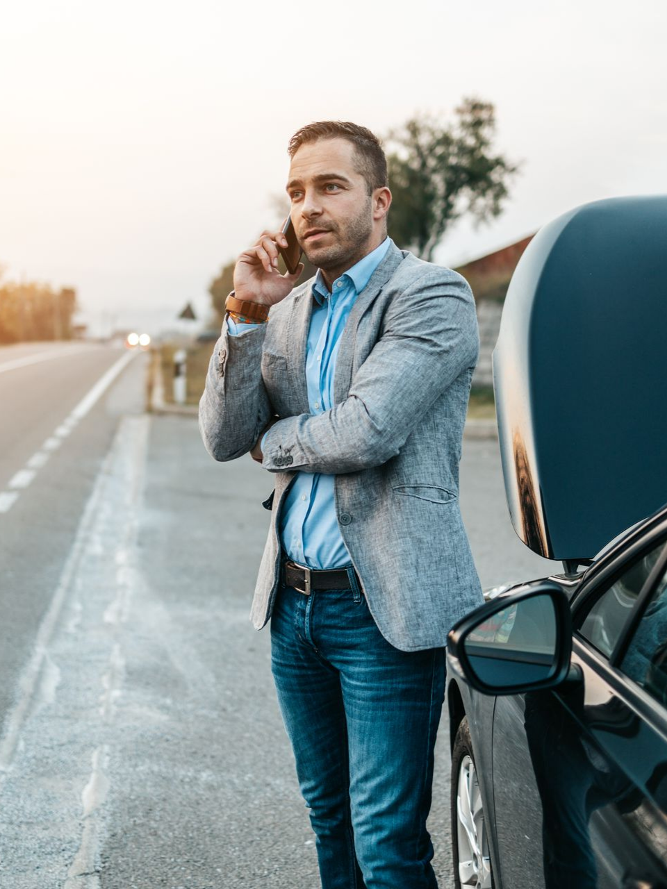 Un homme au téléphone devant sa voiture en panne 