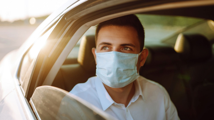 Un homme avec un masque chirurgical regardant par une fenêtre de voiture