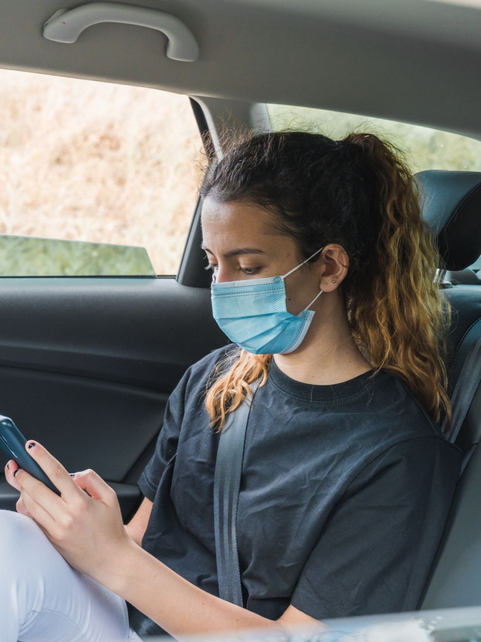 Une femme avec un masque chirurgical à l'arrière d'une voiture avec son Smartphone