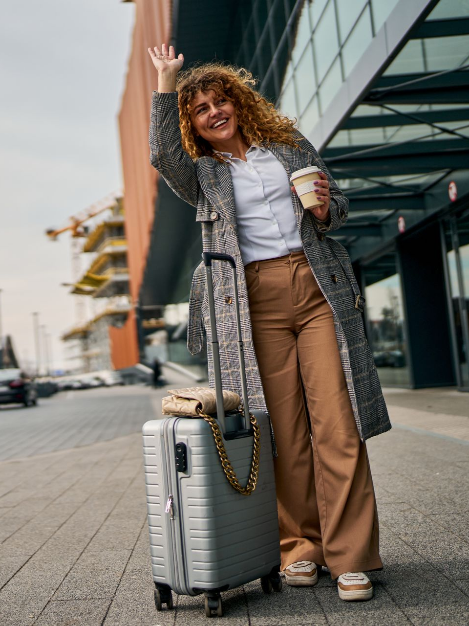 Une femme marchant avec un café et sa valise 
