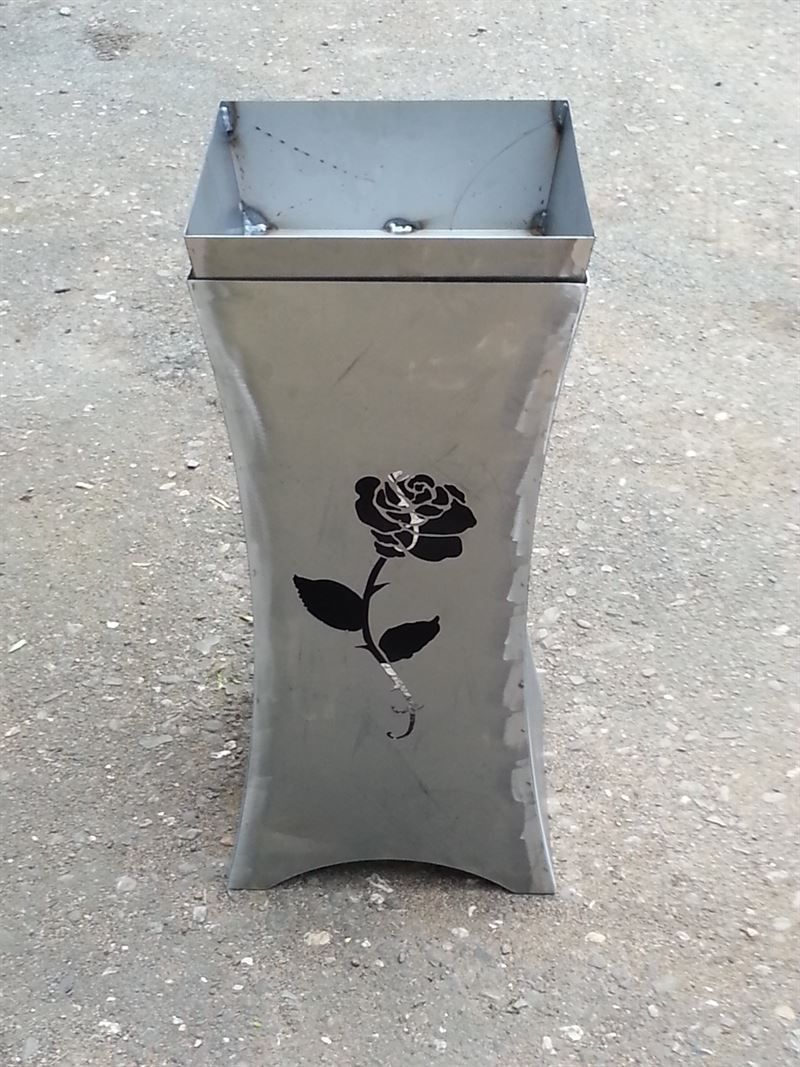 Auf dem Boden steht eine Metallvase mit einer Rose darauf.
