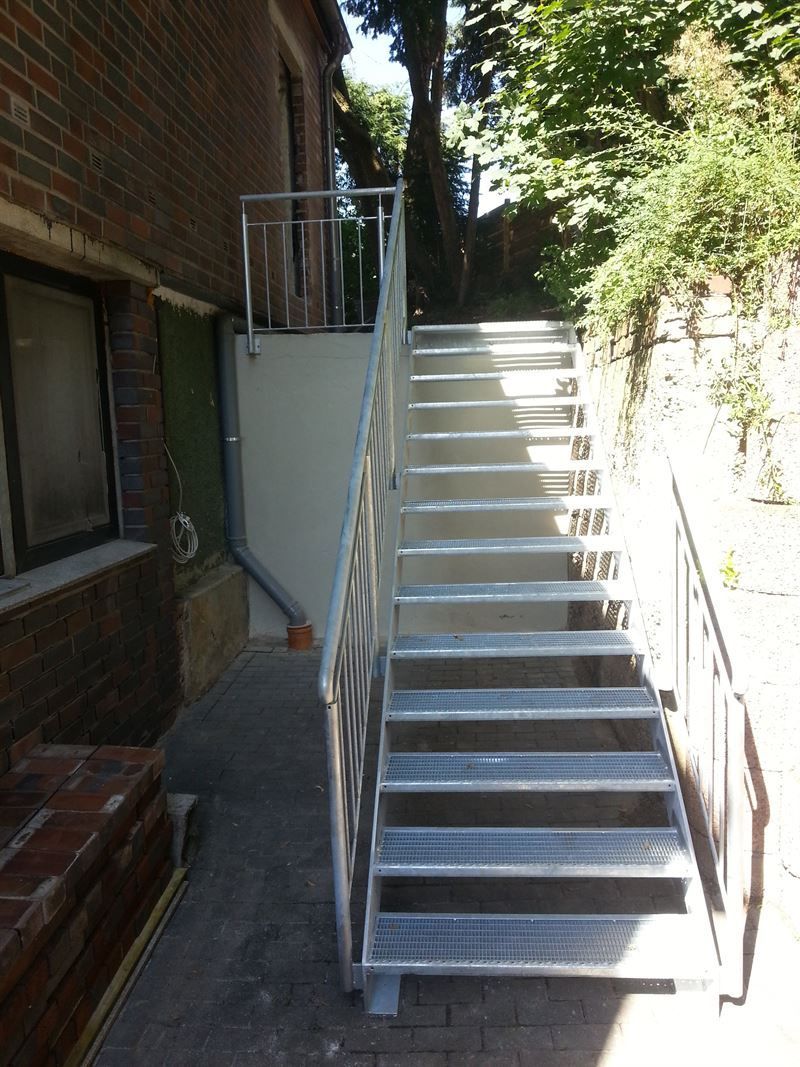 Eine Treppe führt zu einem Backsteingebäude mit Metallgeländer.