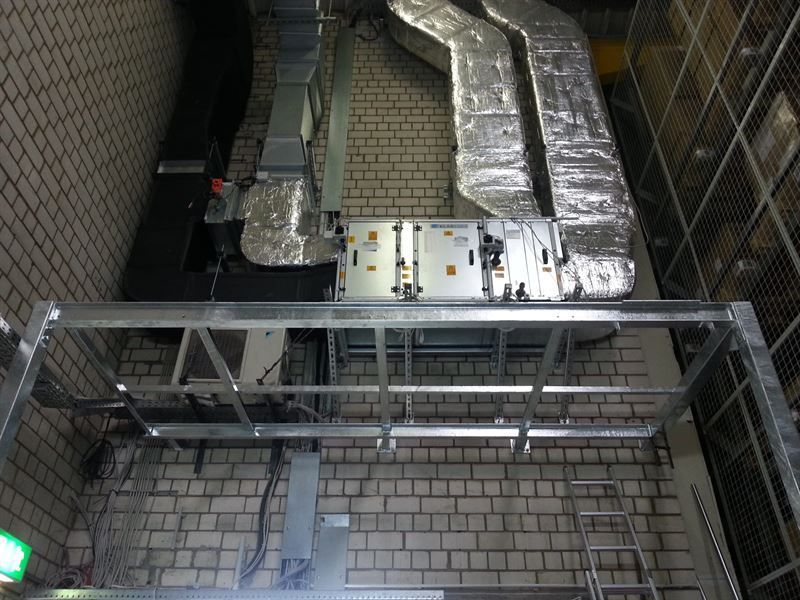 Eine Ziegelwand mit einem Metallrahmen und aus ihr herausführenden Rohren.