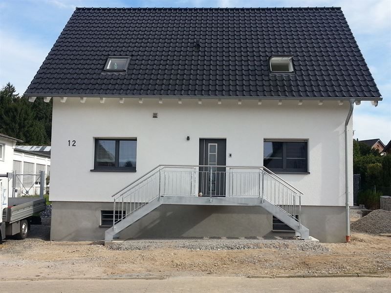 Ein weißes Haus mit schwarzem Dach und Treppen davor.