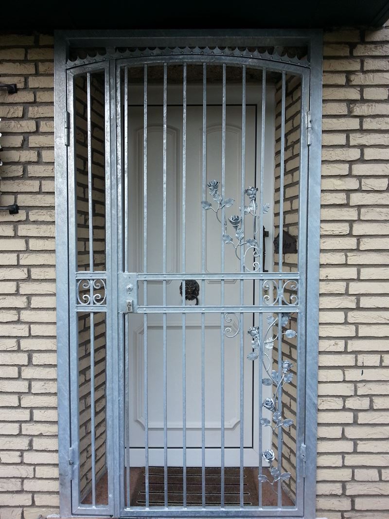 Eine weiße Tür befindet sich hinter einem Metalltor an einer Ziegelmauer
