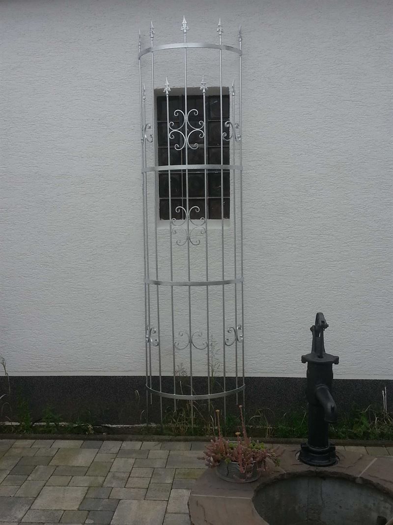 Vor einem weißen Gebäude neben einem Brunnen steht ein Metallgitter.