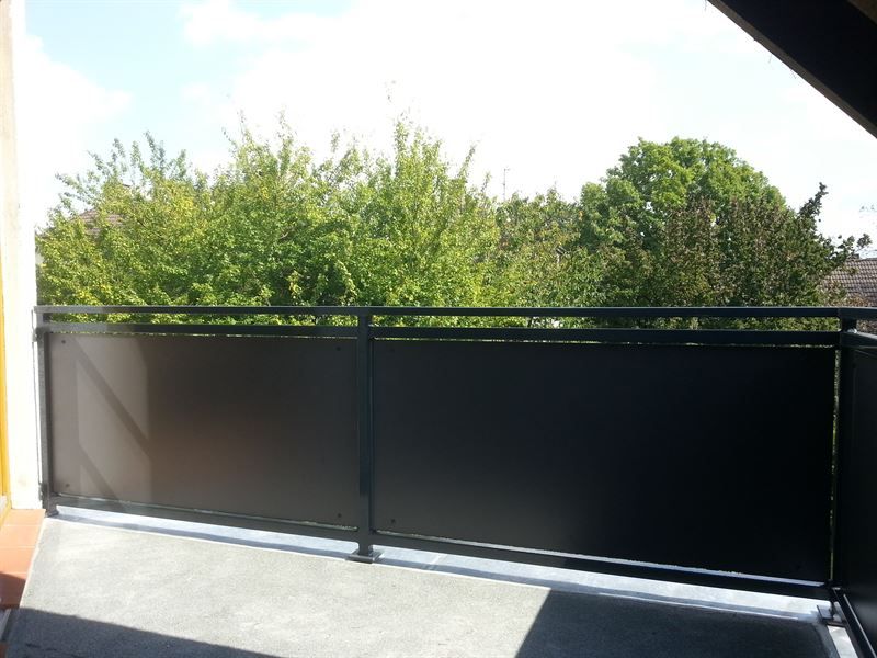 Ein Balkon mit schwarzem Geländer und Bäumen im Hintergrund