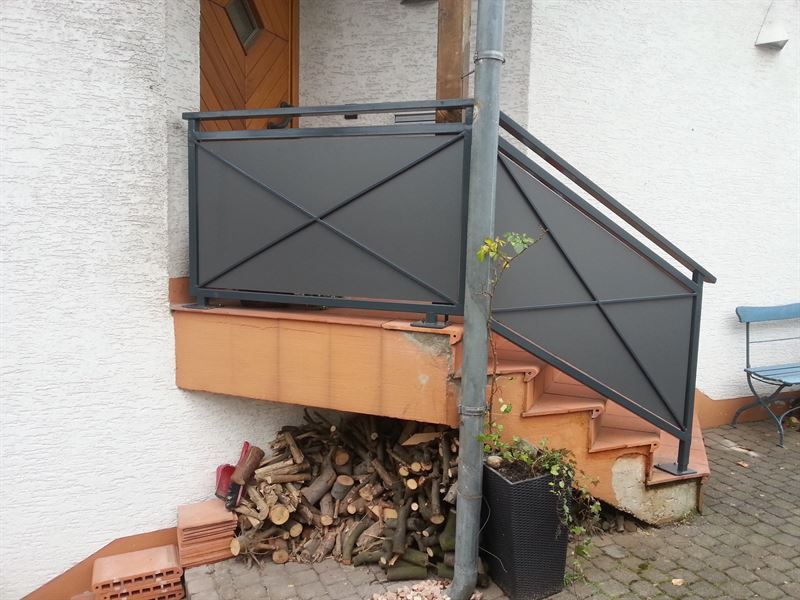 Eine Treppe mit einem schwarzen Geländer ist neben einem Stapel Holz