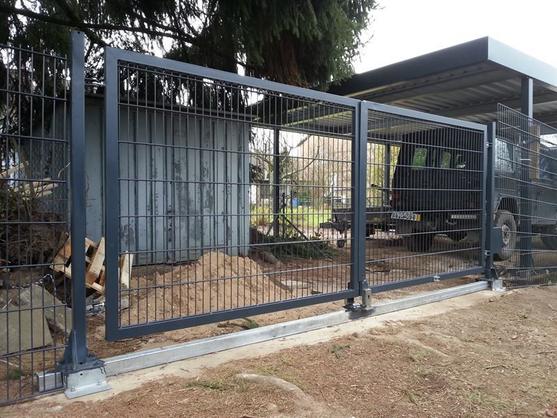 Ein Zaun, unter dem ein Auto und dahinter ein Lastwagen geparkt sind.