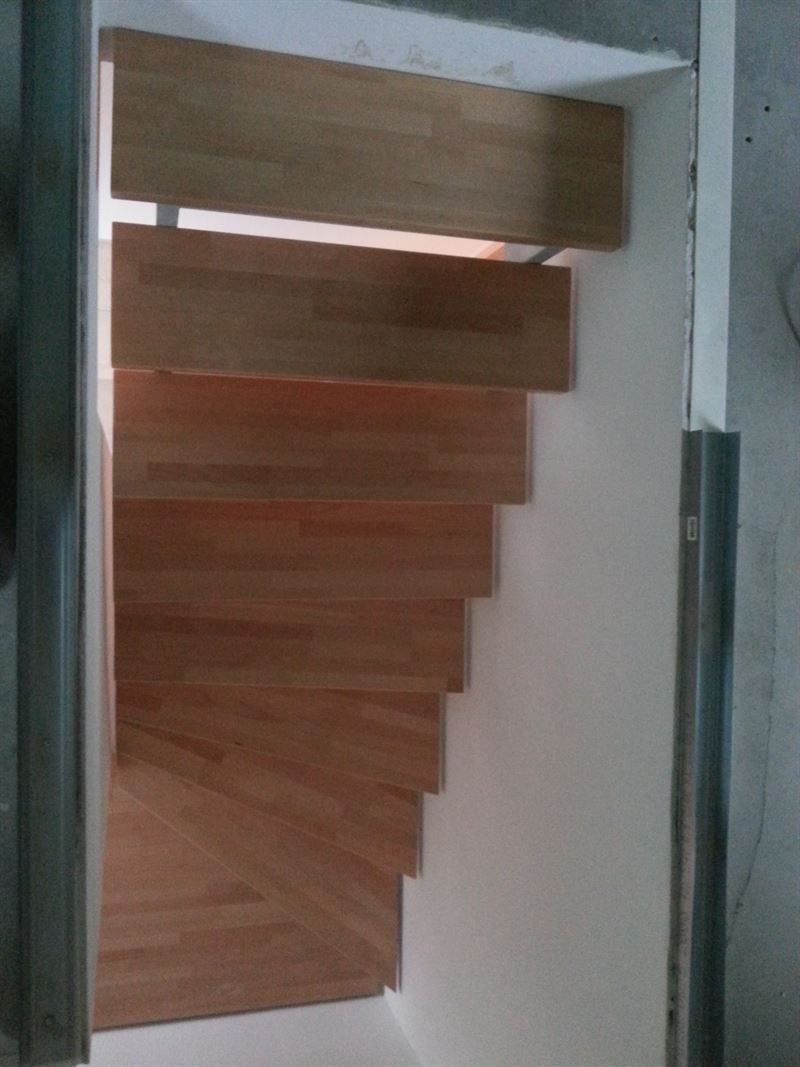 Eine Holztreppe führt eine weiße Wand hinauf.