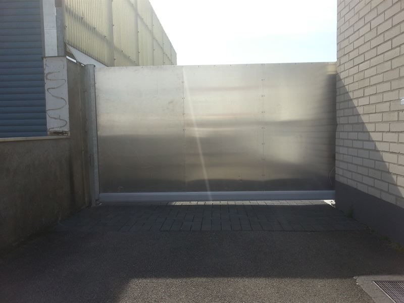 Neben einem Backsteingebäude steht ein Edelstahltor.