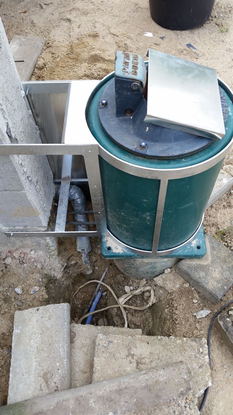 Ein grünes Fass mit einem daran befestigten Spülbecken aus Edelstahl steht im Dreck.