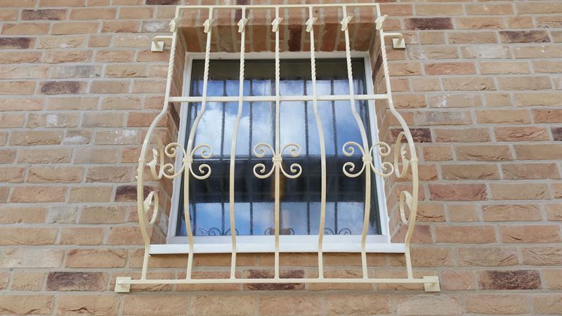 Ein Fenster mit einem schmiedeeisernen Gitter in einer Backsteinmauer.