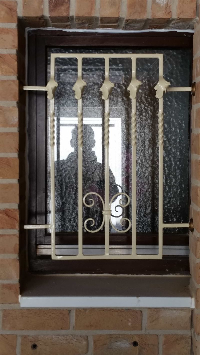 In einer Backsteinmauer befindet sich ein Fenster mit einem schmiedeeisernen Gitter.
