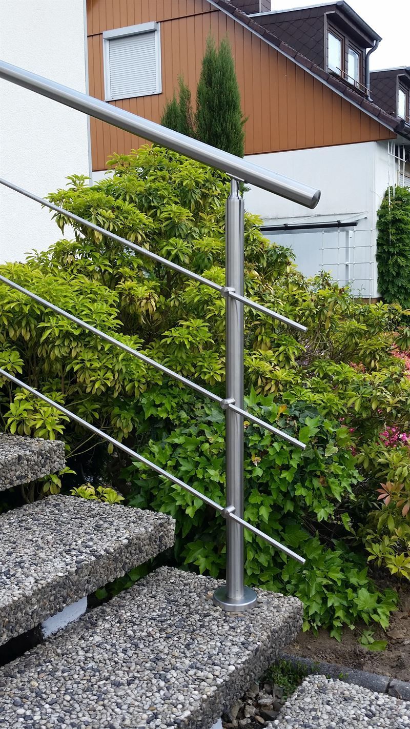 Eine Treppe mit einem Edelstahlgeländer und einem Busch im Hintergrund.