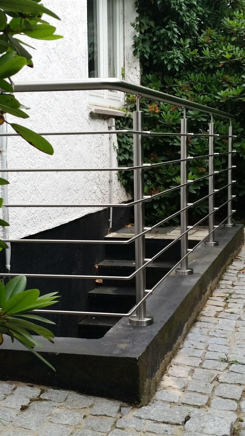Ein Edelstahlgeländer auf einem Gehweg neben einem Haus.