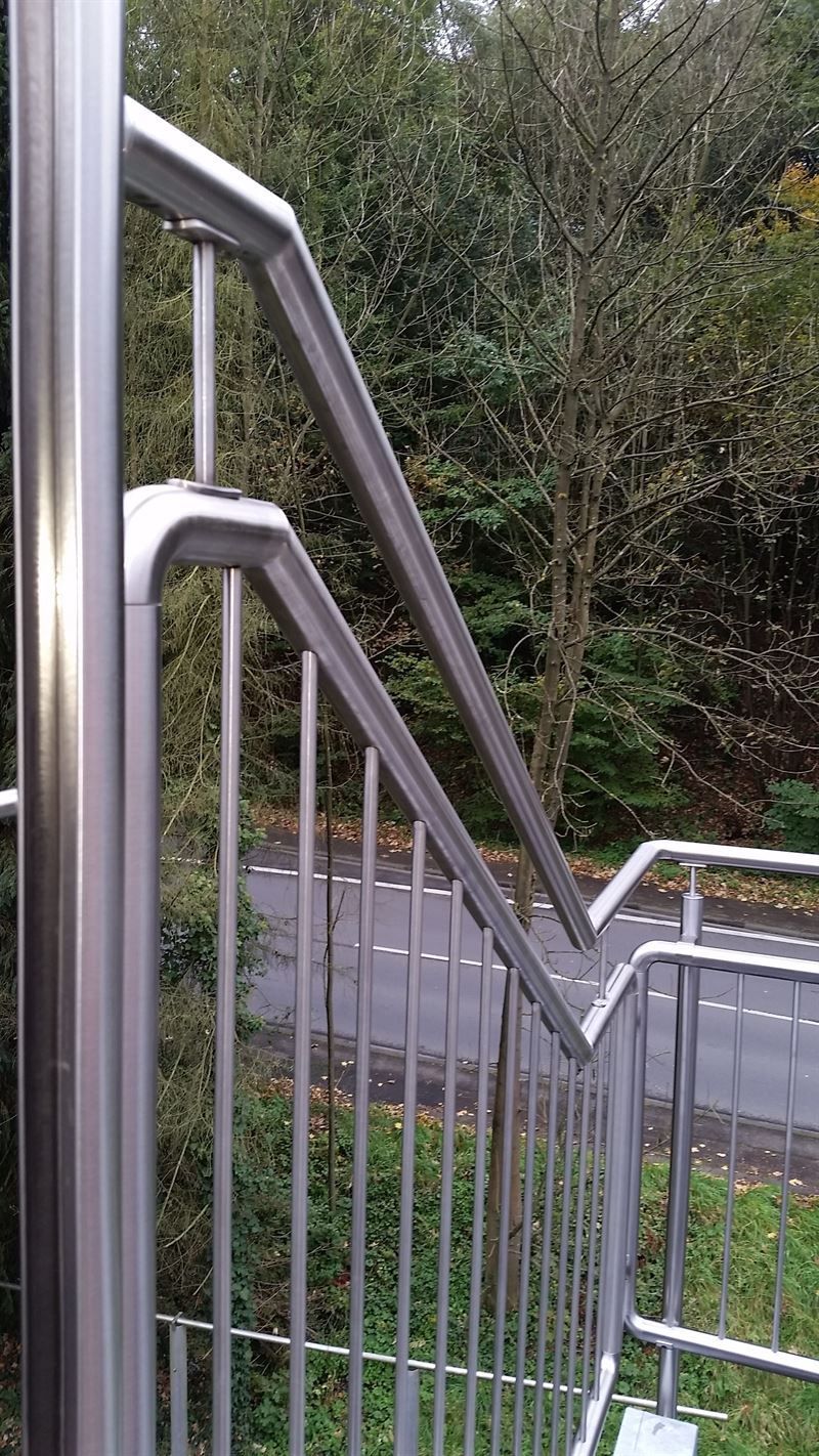 Ein Edelstahlgeländer mit Blick auf eine Straße und Bäume.