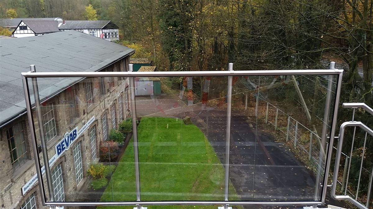 Ein Balkon mit Edelstahlgeländer und Blick auf eine üppige grüne Wiese.