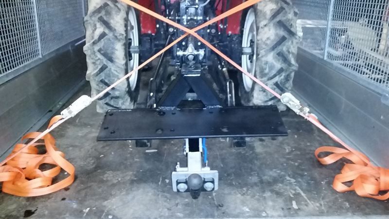Ein Traktor ist mit orangefarbenen Riemen an einem Anhänger festgebunden