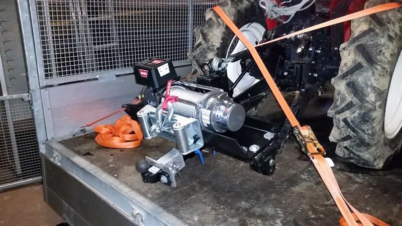 Ein Traktor wird von einem Anhänger mit daran befestigter Seilwinde gezogen.