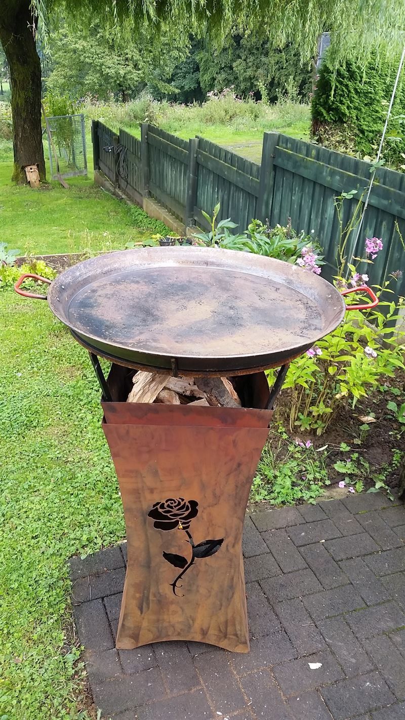 Auf einer gemauerten Terrasse neben einem Zaun steht eine Feuerstelle.