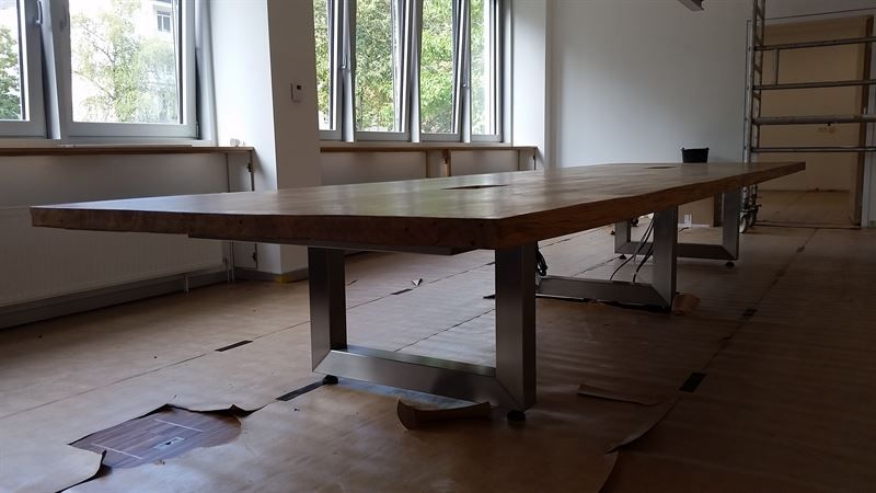 In einem Raum mit vielen Fenstern steht ein langer Holztisch.