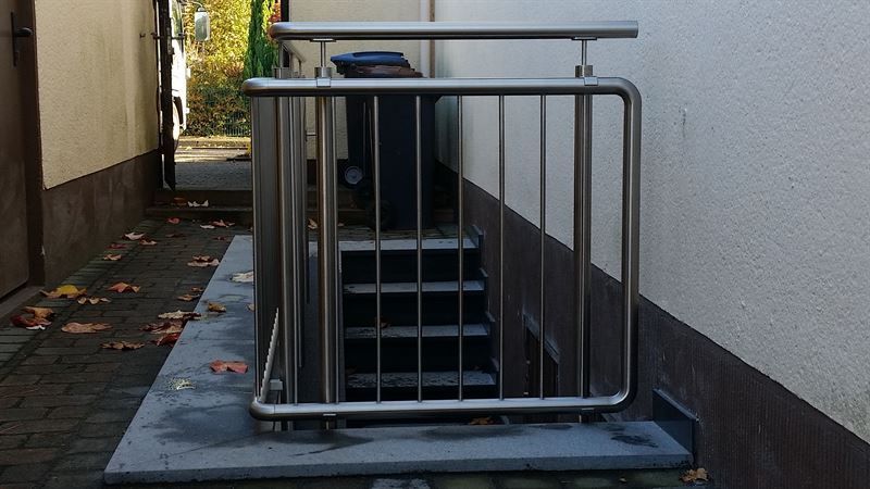 Eine Treppe mit Edelstahlgeländer und im Hintergrund ein Mülleimer.
