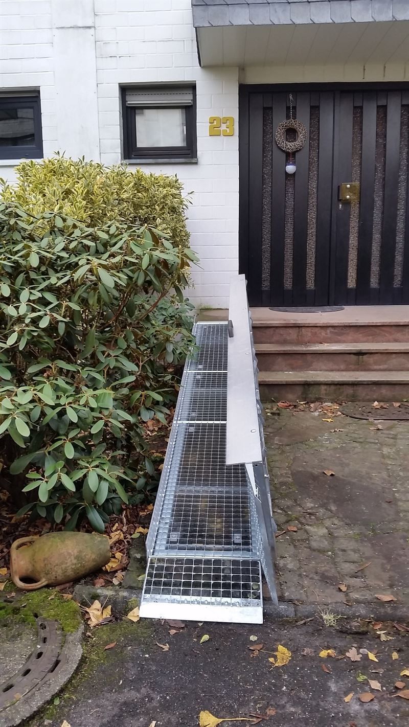 Vor einem Haus mit einer schwarzen Tür steht eine Leiter.