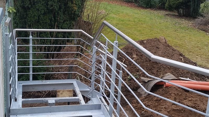 Auf einem Erdhügel steht eine Metalltreppe mit Geländer.