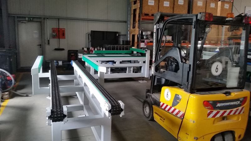 Ein gelber Gabelstapler steht in einer Lagerhalle neben einem Förderband.