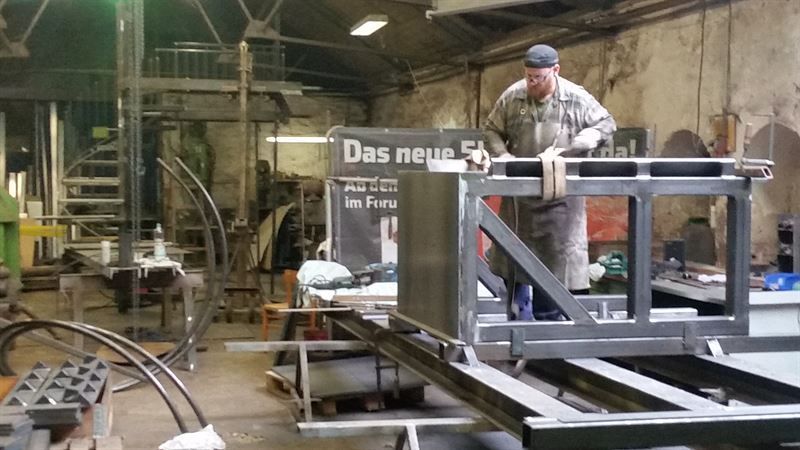 Ein Mann arbeitet an einem Stück Metall in einer Fabrik mit einem Schild mit der Aufschrift „Das neue
