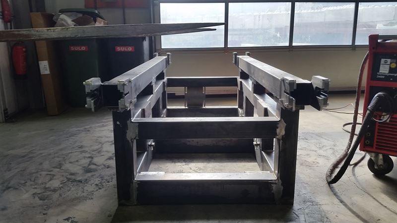 In einer Lagerhalle steht eine Metallkonstruktion neben einer Schweißmaschine.