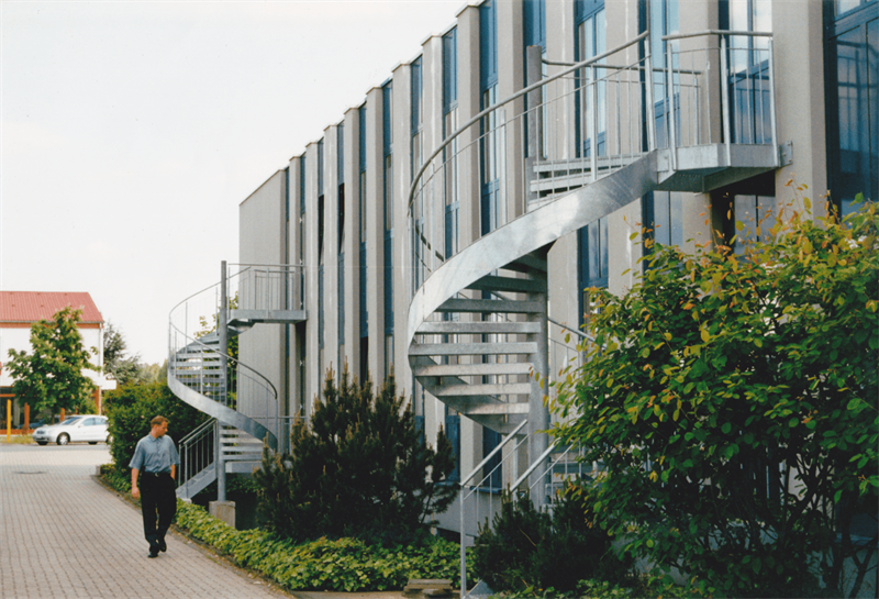 Ein Mann geht einen Bürgersteig vor einem Gebäude mit einer Wendeltreppe entlang