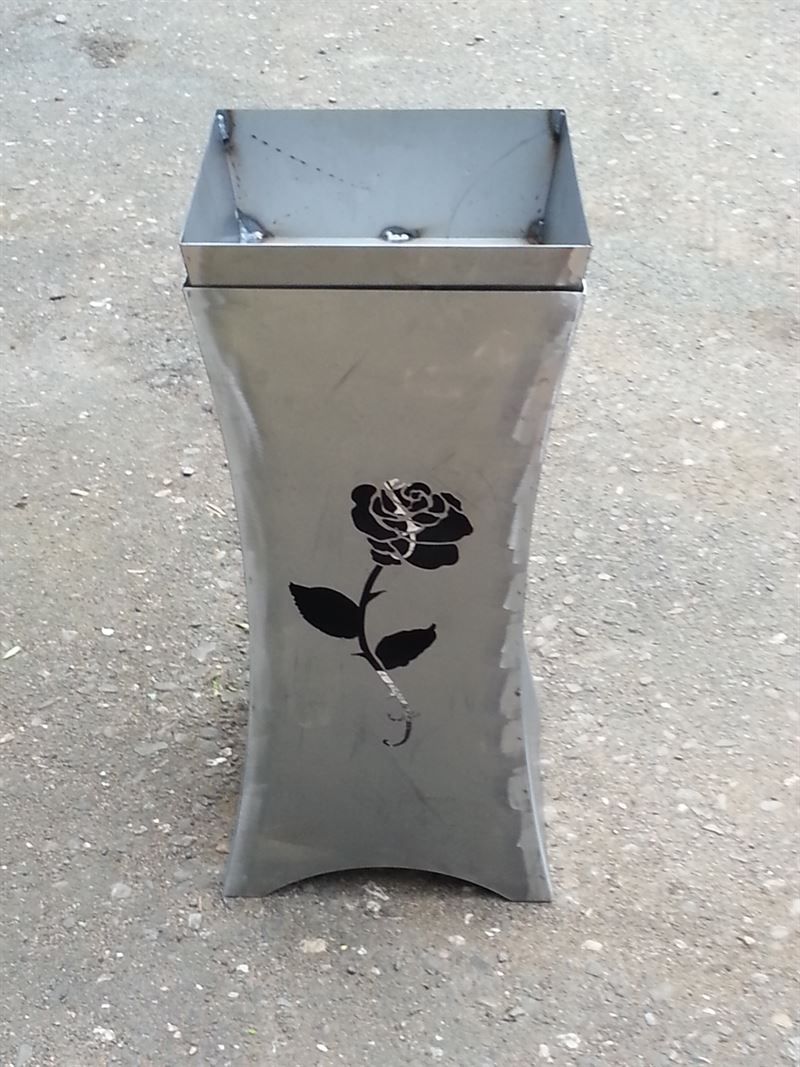 Auf dem Boden steht eine Metallvase mit einer Rose darauf.