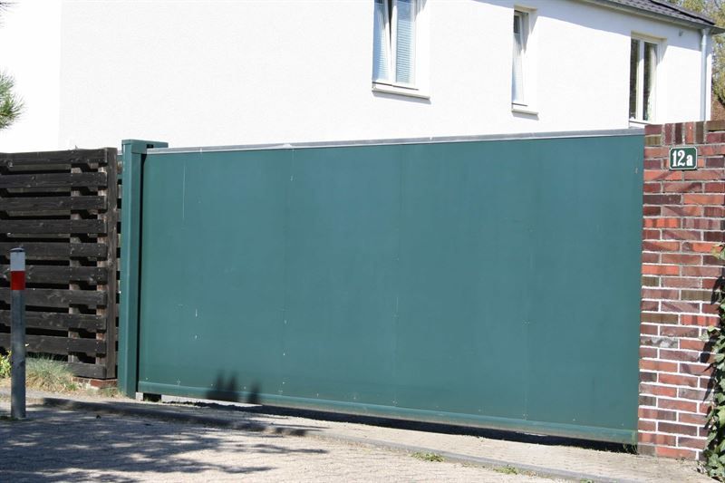 Vor einem weißen Haus ist ein grünes Schiebetor geschlossen.
