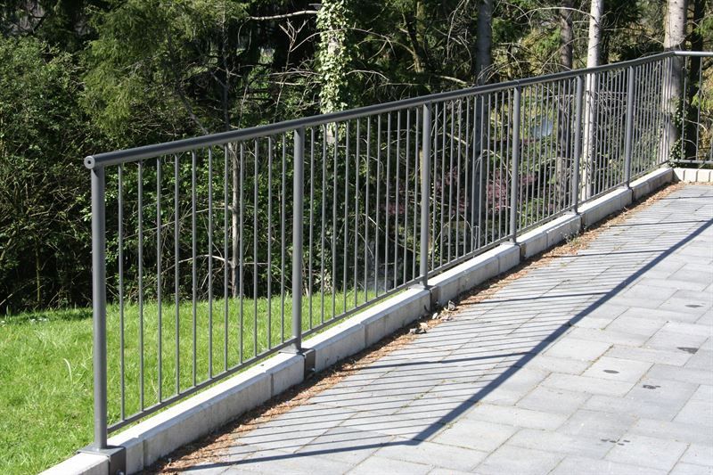 Ein Metallzaun entlang eines Gehwegs mit Bäumen im Hintergrund
