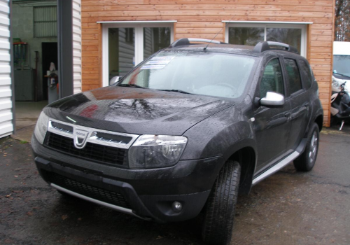 Un SUV noir garé devant une maison en briques, dans une allée mouillée